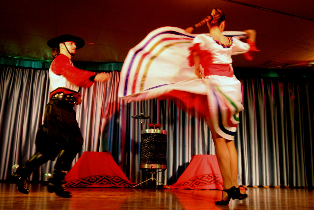 areja de danza folclórica en Río Grande do Sul con bailarín de chula usando espuelas gauchas tradicionales y mujer con falda en movimiento.