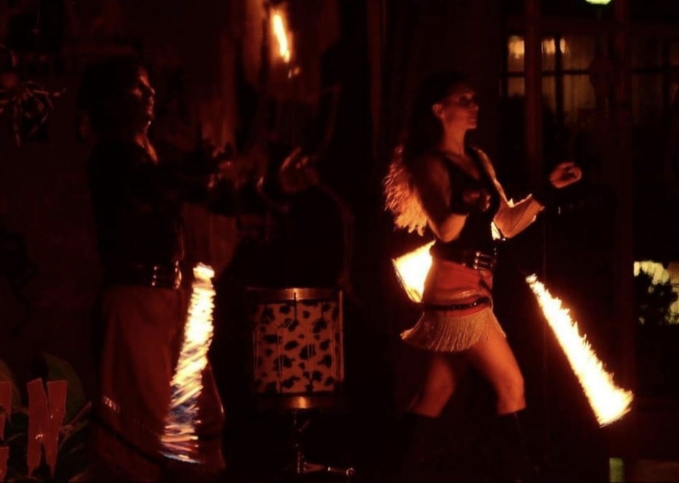 Milton y Gala realizando un espectáculo de fuego al aire libre con boleadoras y llamas de gran alcance durante un festival exterior.